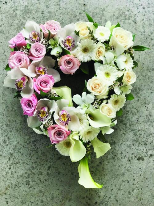A 12" open heart so full of flowers, it almost appears to be soild. soft pink roses, white roses, white calla lilies, white cymbidium orchid blooms, white dendrobium orchids, white waxflower, and white gerberas rest amongst Italian ruscus.