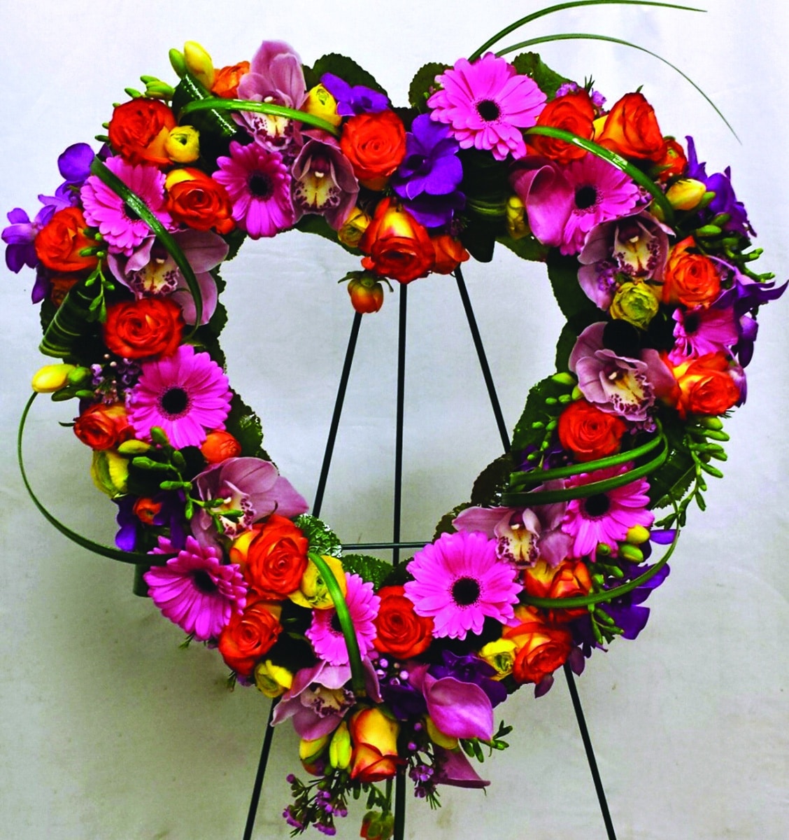 A bright and colourful open heart design made with pink calla lilies, orange roses, pink gerbera, yellow freesia, yellow ranunculus, orange ranunculus, purple dendrobium orchids, pink waxflower, pink cymbidium orchids, and lily grass.