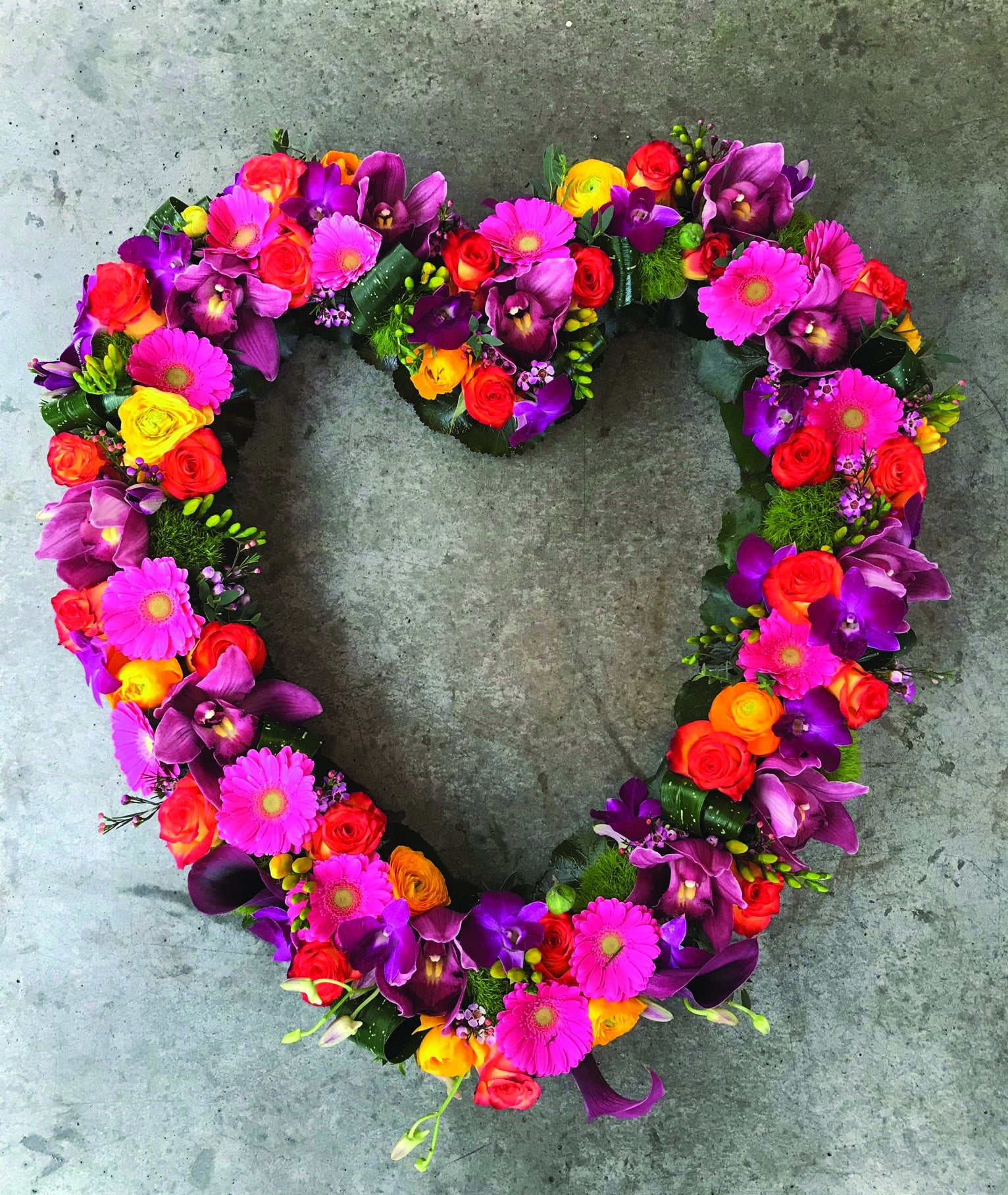 A bright pink, purple and orange open heart design. Made with orange roses, pink cymbidium orchids, hot pink gerberas, yellow freesias, dianthus, yellow rununculus, puple dendrobium orchids, and dark pink calla lilies.