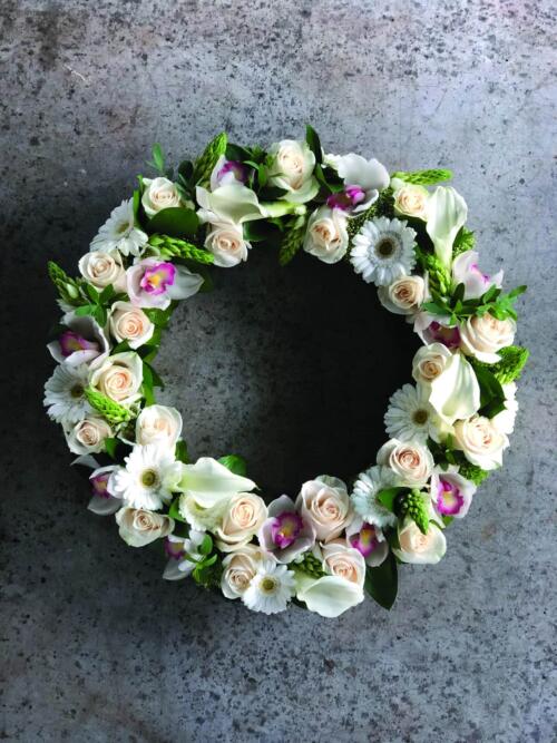 A gorgeous white and soft pink flowered wreath with roses, cymbidium orchid blooms, calla lilies, gerbera daisies, and star of Bethlehem.