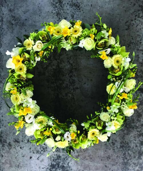 A large yellow and white wreath with roses, cymbidium orchids, lisianthus, bells of ireland, dendrobium orchids, and freesia.