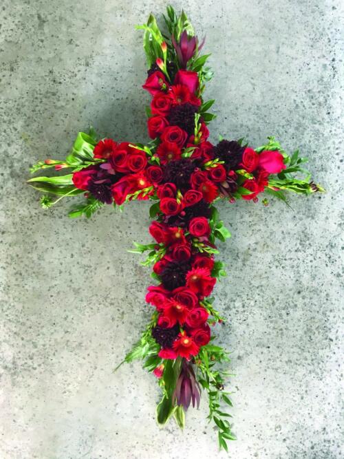 A red cross shaped floral arrangment featuring roses and dahlias.