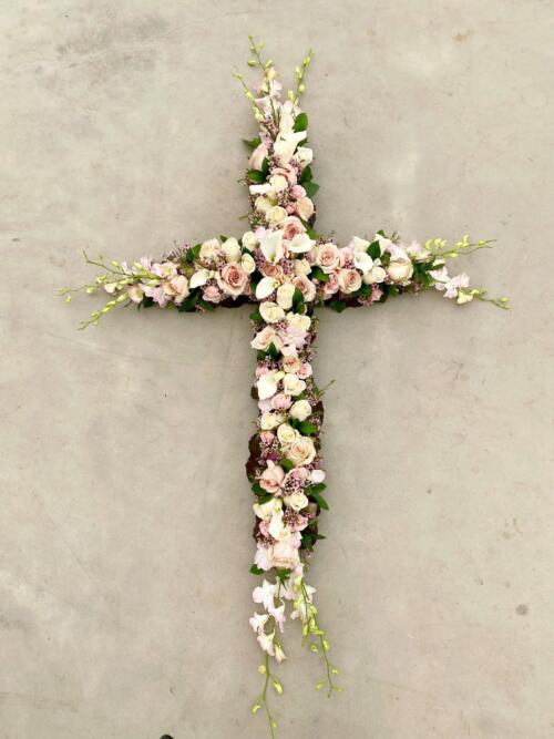 A large soft pink and white flowered cross featuring roses, cymbidium orchids, dendrobium orchids, and calla lilies.