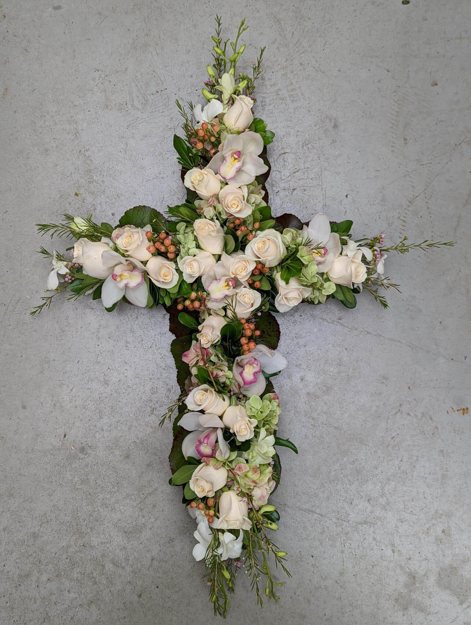 A blush and white floral cross featuring hydrangea, roses, and cymbidium orchids.