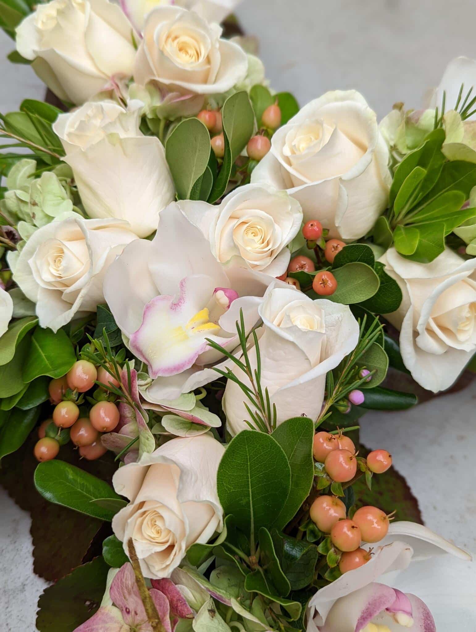 Close up of white roses, white cymbidium orchids. and peach hypericum in a floral cross.