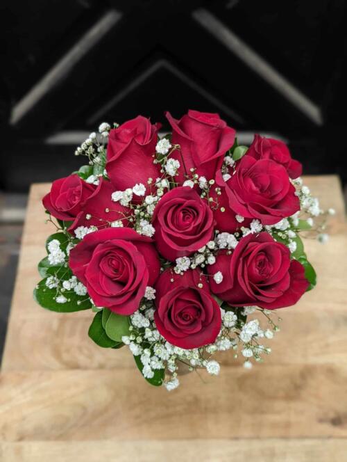 A small bouquet of roses with baby's breath and minimal green wrapped with satin in a glass vase.