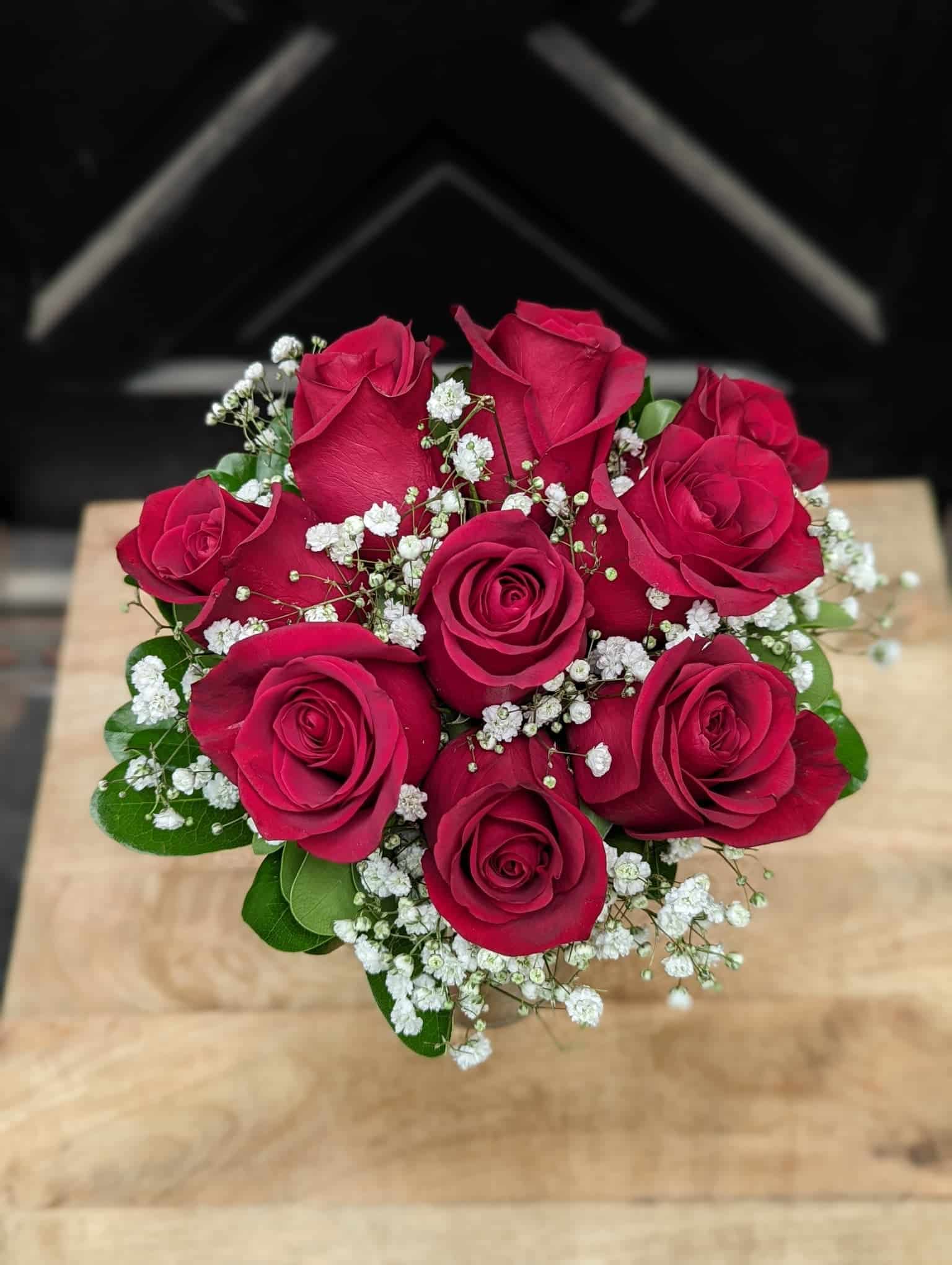 A small bouquet of roses with baby's breath and minimal green wrapped with satin in a glass vase.