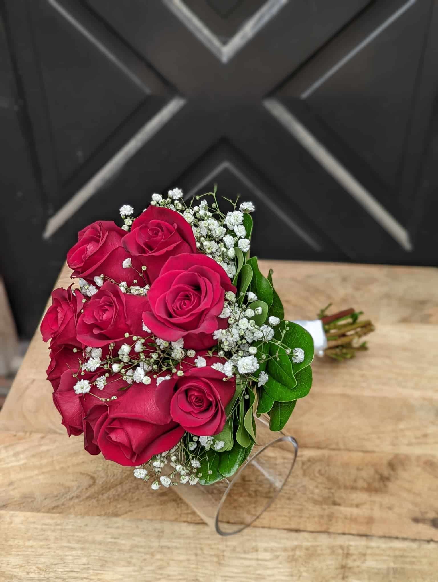 A red rose bouquet with baby's breath and minimal green wrapped in stain laying on a table.