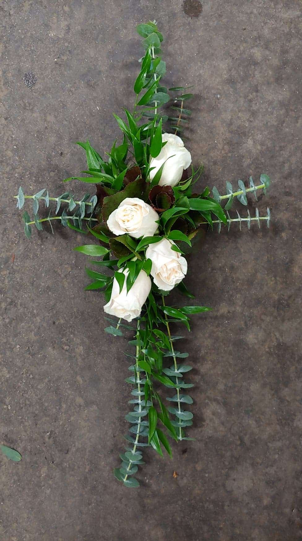 Baby blue eucalyptus and ruscus in the shape of a cross with four white roses.