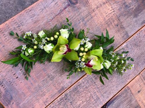 A small garland of ruscus, white hypericum, white spray roses, and green cymbidium orchids.
