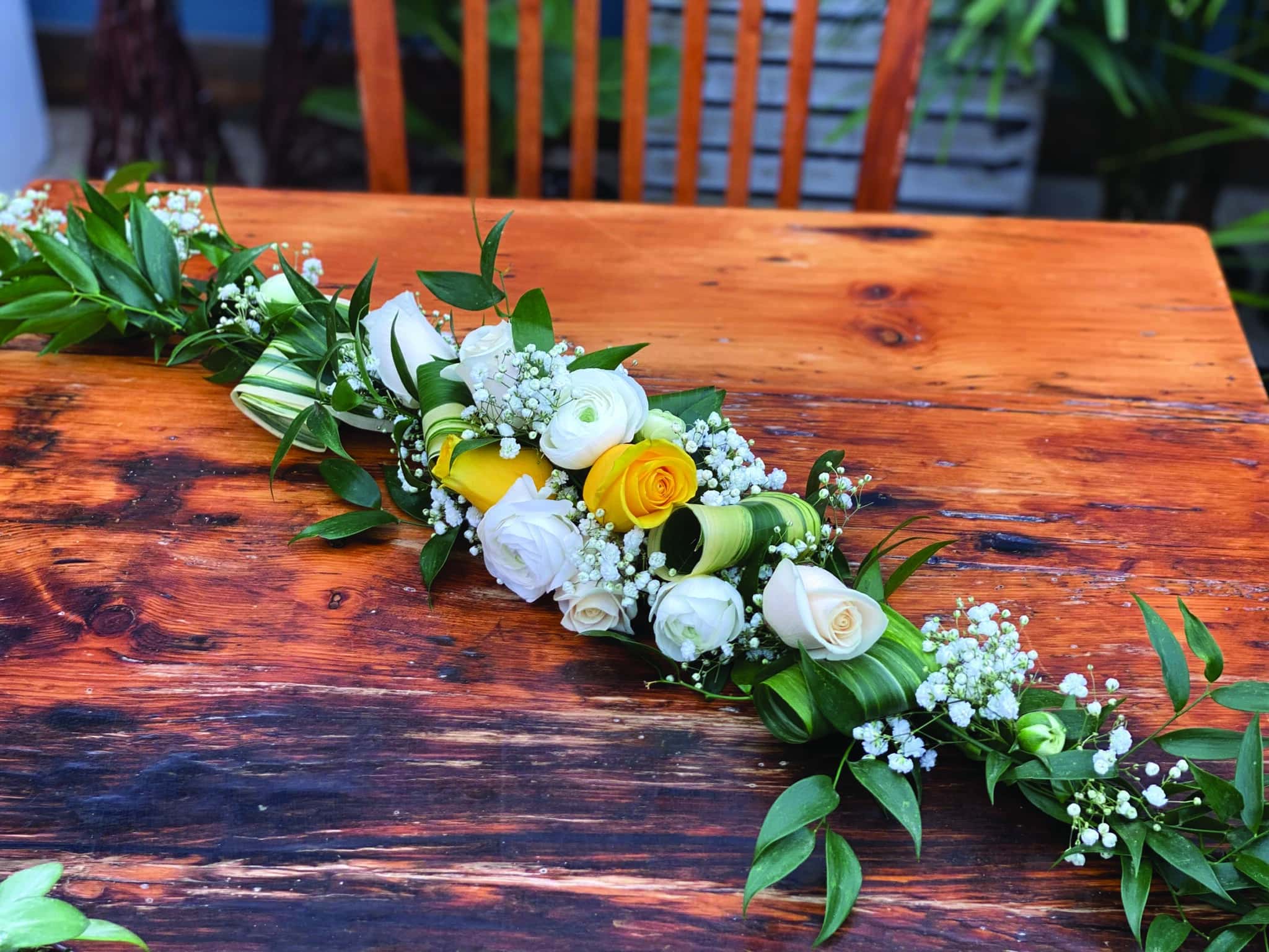 A garland of white roses, yellow roses, white rununculus, baby's breath, aspidestra, and ruscus.