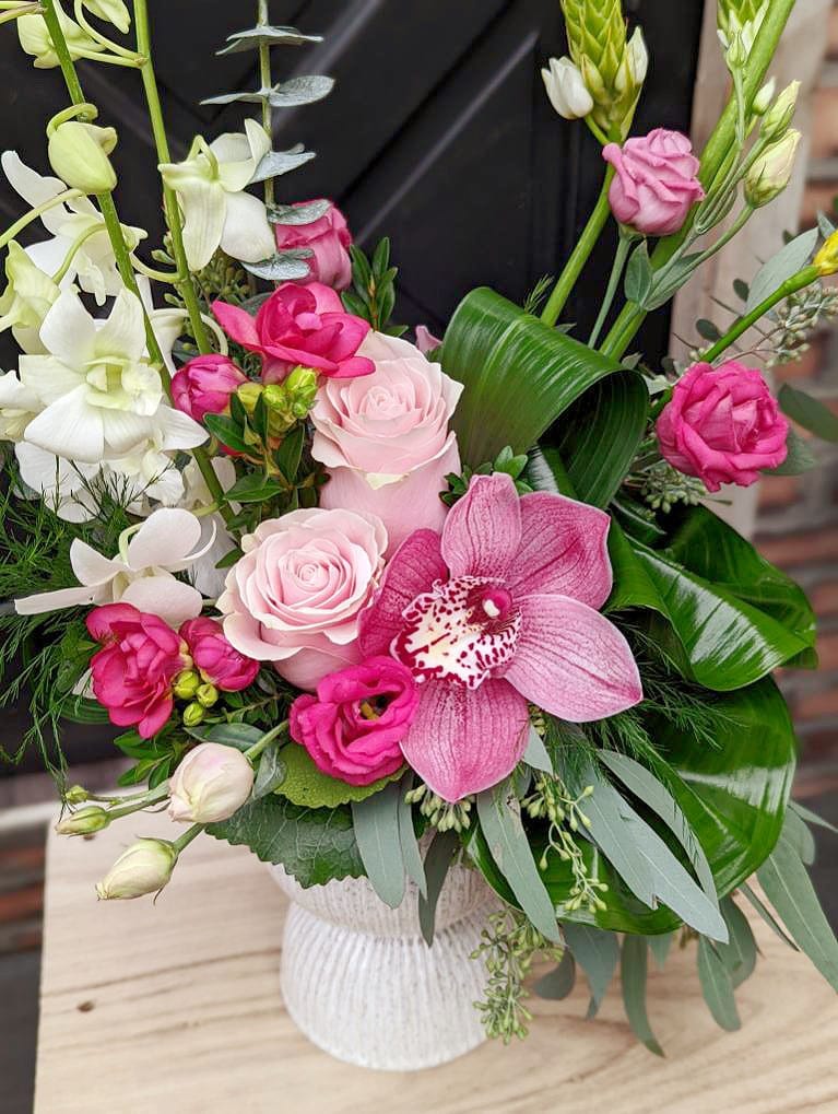 A tall pink European style floral arrangement in a white ceramic pedestal vase.