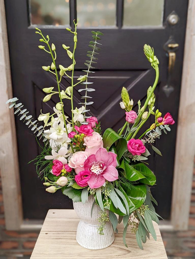 A tall pink European style floral arrangement in a white ceramic pedestal vase.