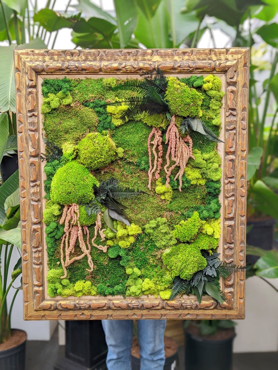 A large piece of moss art in varying shades of green presented in a carved wooden frame.