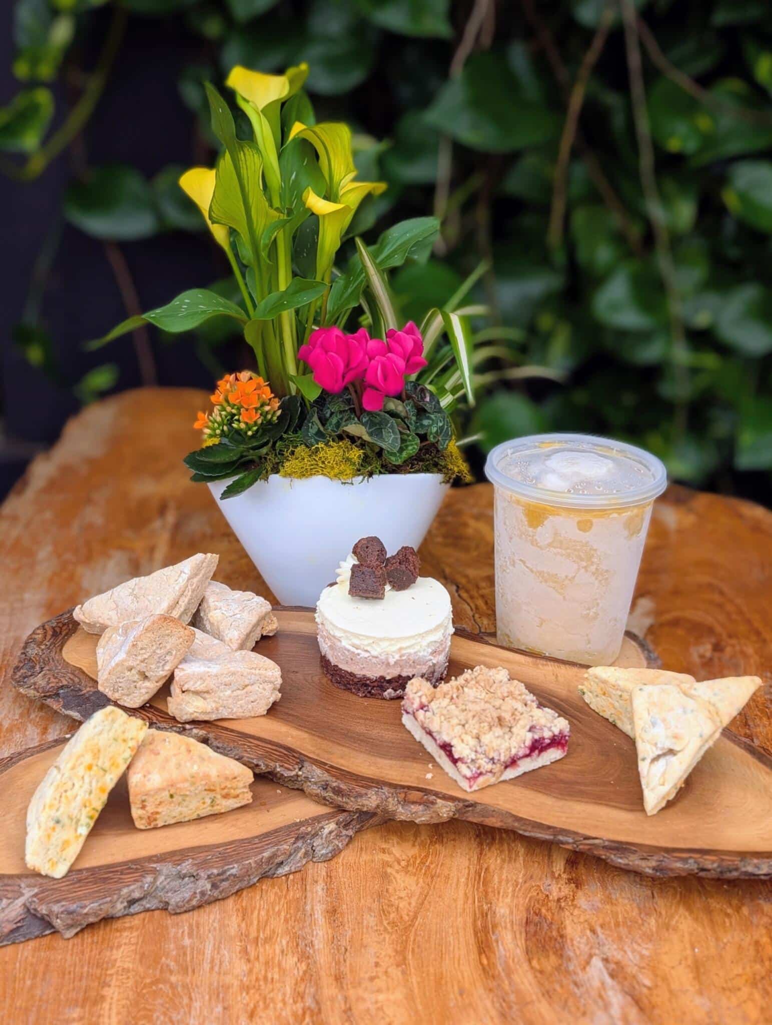 The Gluten Friendly Cheer Collection from The Watering Can Flower Market, showing a kraft bakery box, house-made gluten-friendly pastries, and beverages on a wooden board.