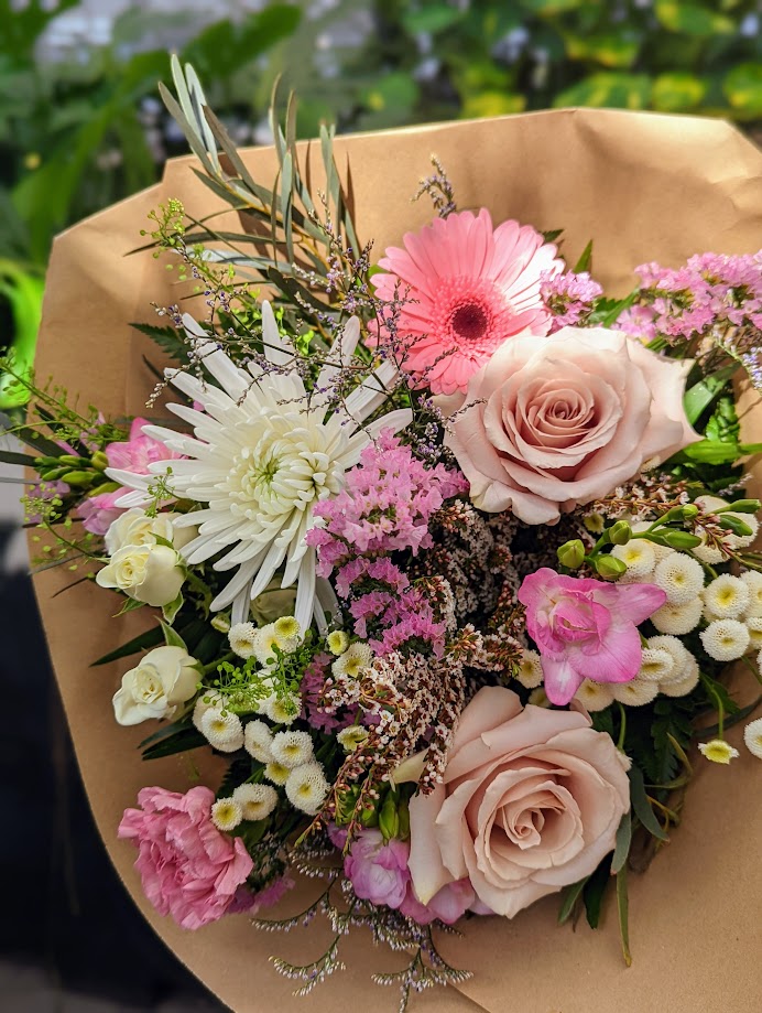 Close-up of a kraft-wrapped bouquet with blush roses, pink gerbera, white spider mum, statice and small white daisies.