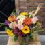A colourful autumn bouquet in a glass vase with yellow gerbera daisies, an orange chrysanthemum, pink roses, white hydrangea and wheat.