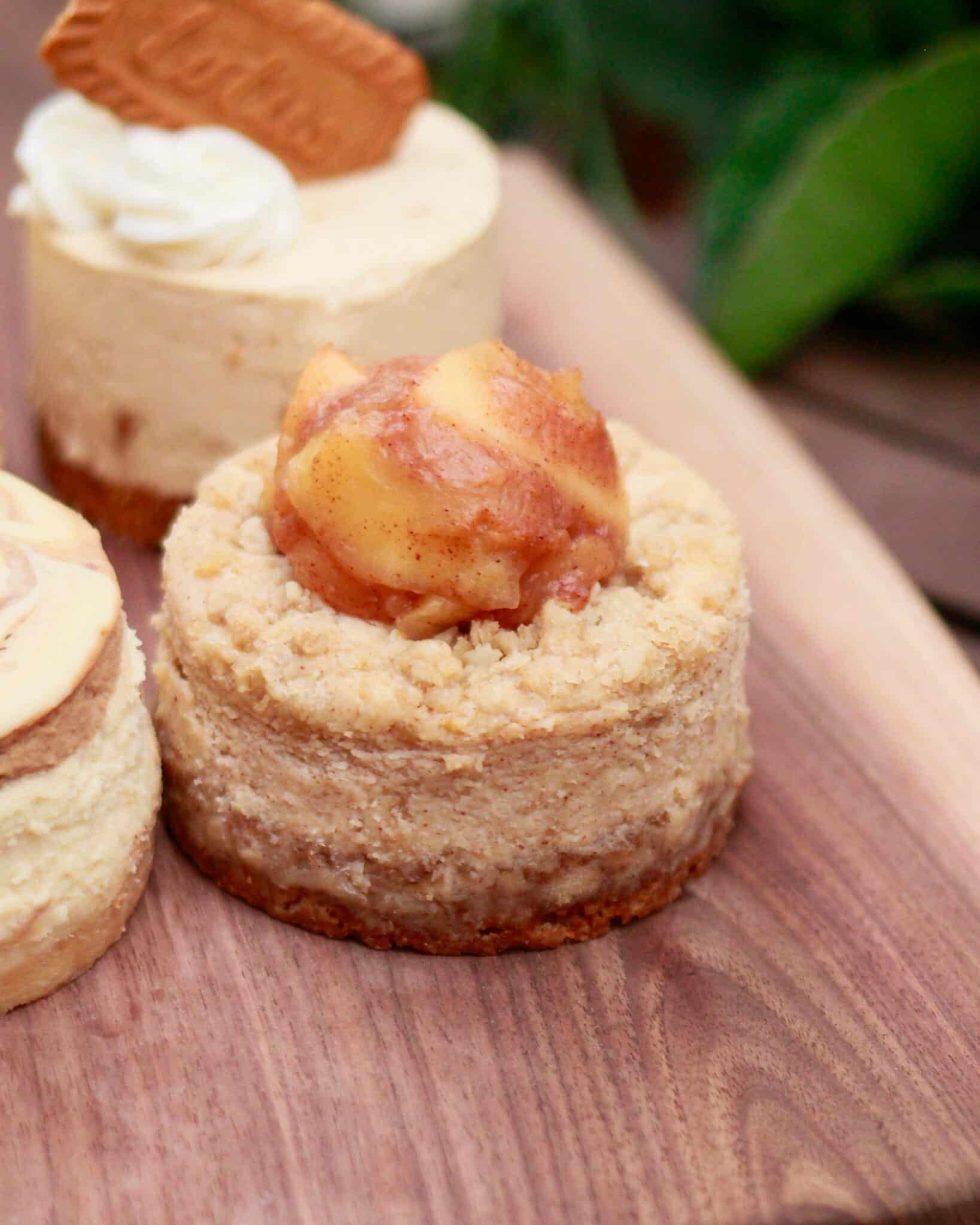 Close-up of a mini cheesecake with a crumble crust and caramelized apple topping on a wooden board.