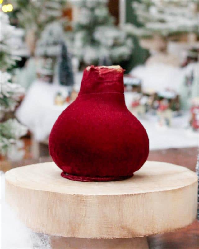 A waxed amaryllis bulb wrapped in deep burgundy velvet, displayed on a wood slice in a festive setting.