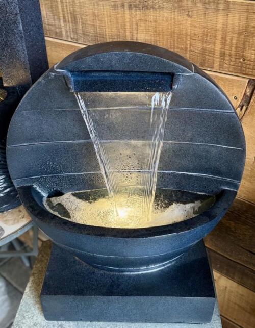 A rounded dark fountain with water sheeting over a curved lip into a glowing bowl.