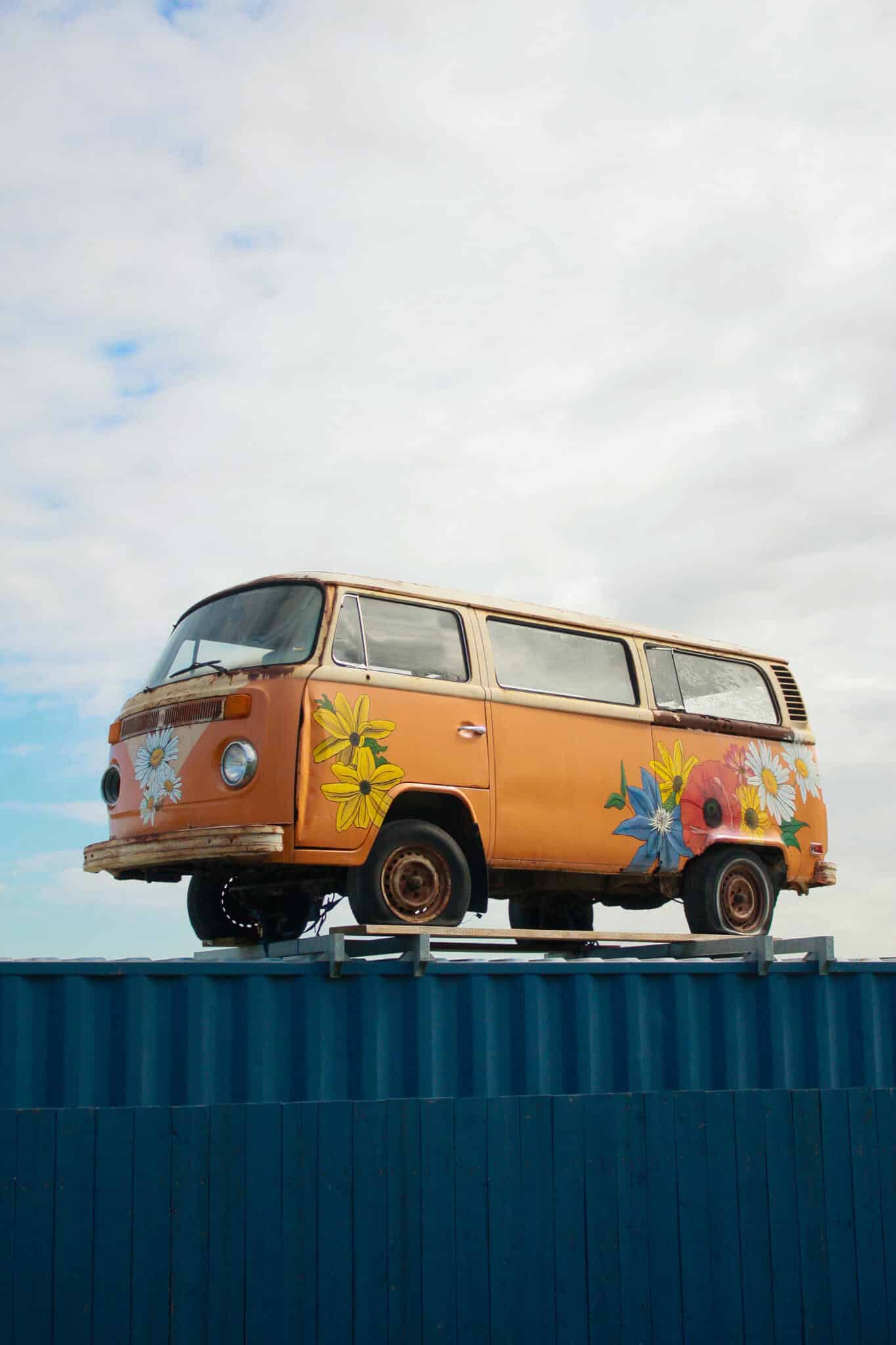 The Watering Can Vintage VW Bus — Flower-Painted Exterior A vibrantly painted orange and yellow Volkswagen T2 bus adorned with colourful flower designs, parked on the property of The Watering Can Flower Market in Vineland.