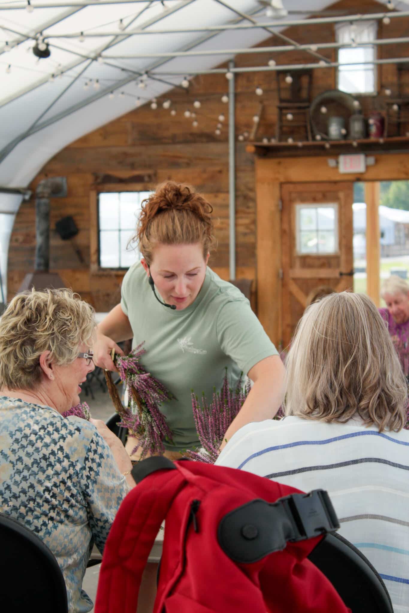 Floral Workshop Instructor Helping Guests at The Watering Can A floral workshop instructor leans over a worktable, guiding participants through a hands-on workshop at The Watering Can Flower Market's Workshop Village in Vineland.