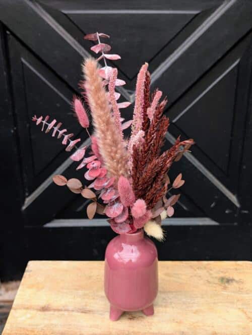Dried arrangement of pink and burgundy grasses, pink eucalyptus and bunny tails in a dusty pink footed vase.