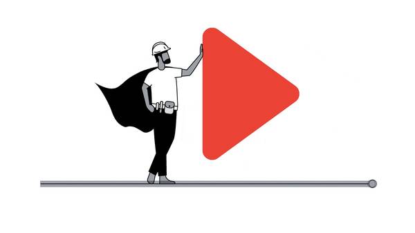 A man wearing a white t-shirt, black trousers, a cape, hard hat, and toolbelt is standing, leaning on one hand against an oversized YouTube play icon.