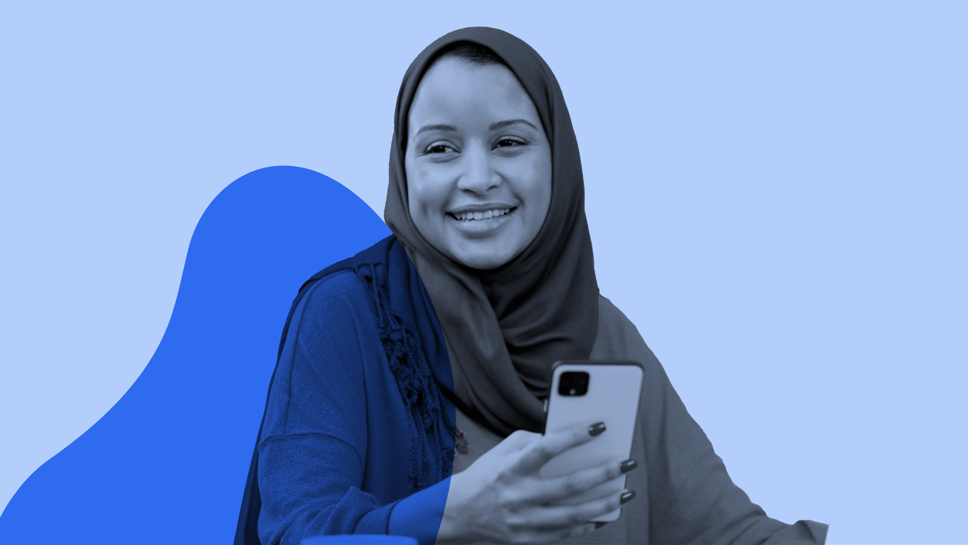 A woman of colour wearing a hijab smiles as she holds her smartphone.