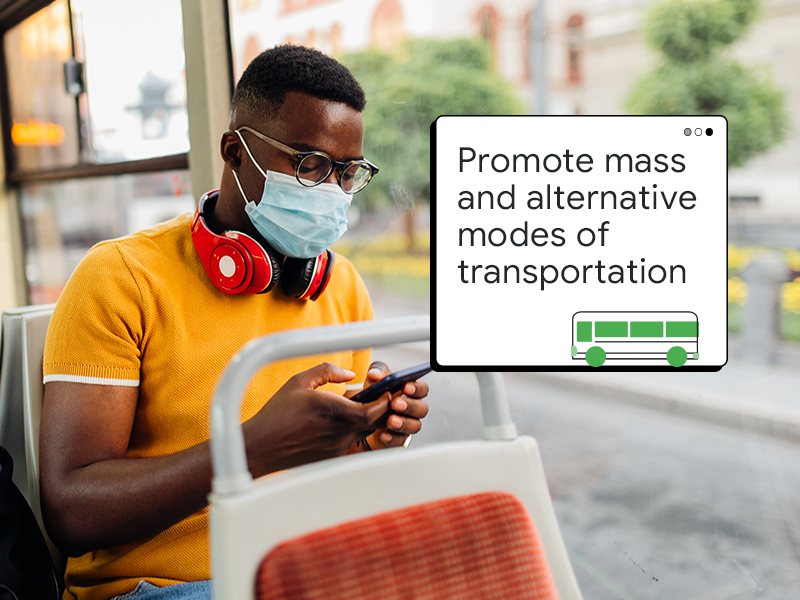 A man with dark skin and hair, wearing glasses and a surgical mask over his mouth and nose, uses a mobile device while riding a city bus. A pop-up window reads “Promote mass and alternative modes of transportation.”
