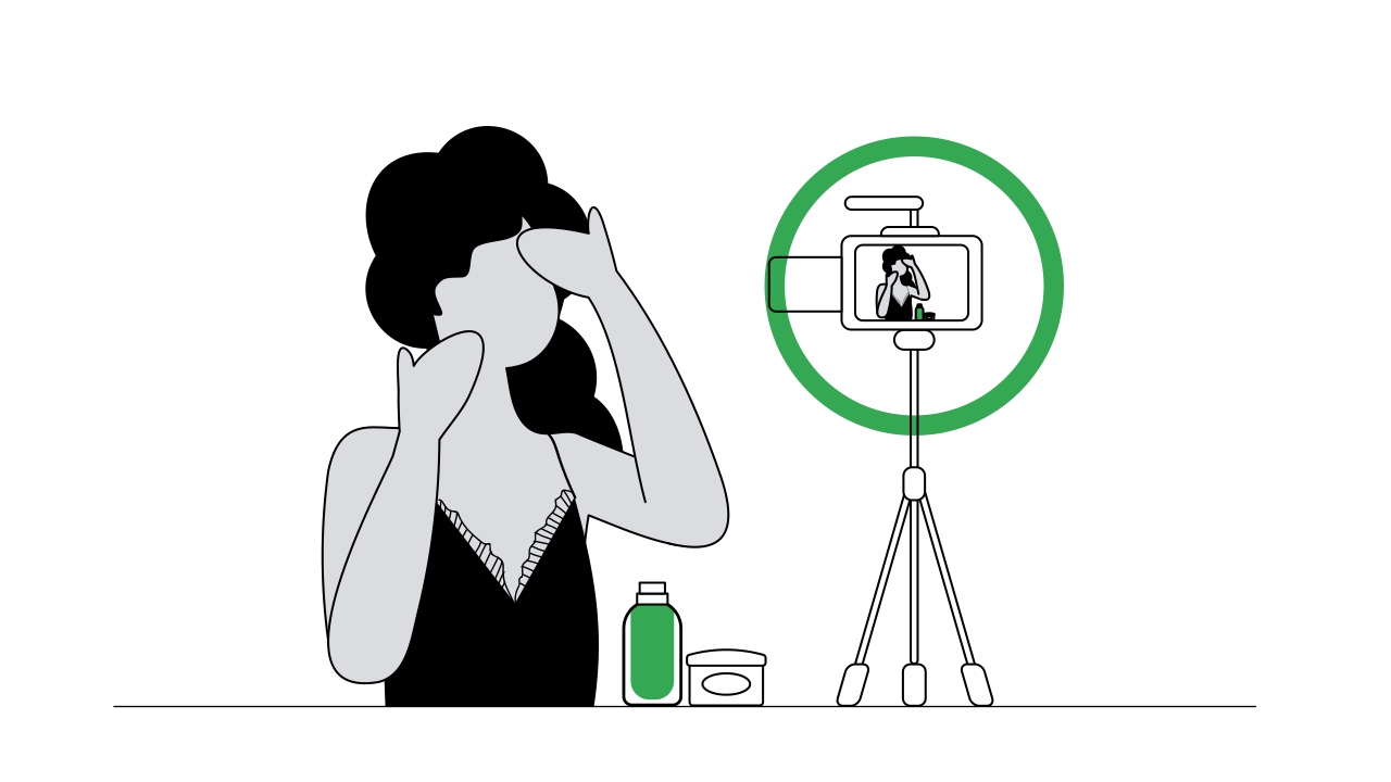 Una mujer de cabello oscuro y rizado, en pijama, se toca con ambas manos el rostro. Frente a ella, un trípode con un dispositivo móvil y una luz con círculo verde.