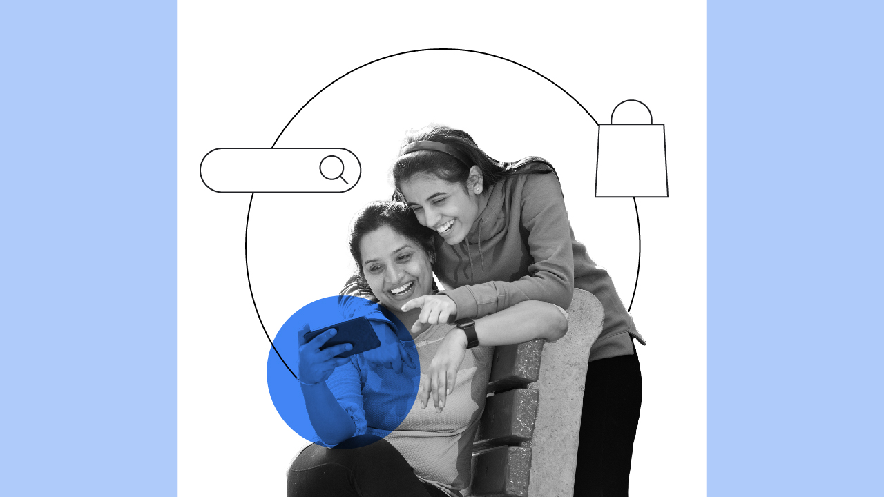 Two women smiling while shopping online on a mobile phone during the mega sale season.