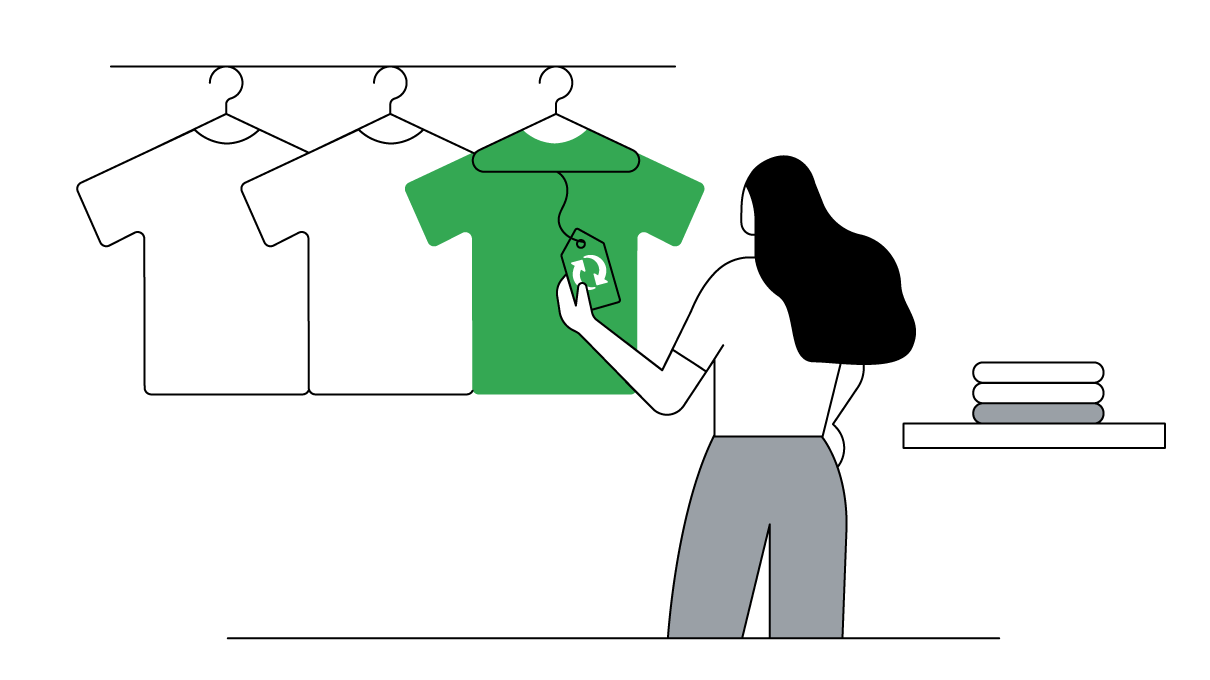 Mulher de cabelos escuros segura a etiqueta de uma camiseta verde, que está pendurada com outras camisetas, só que brancas, em uma arara de uma loja.