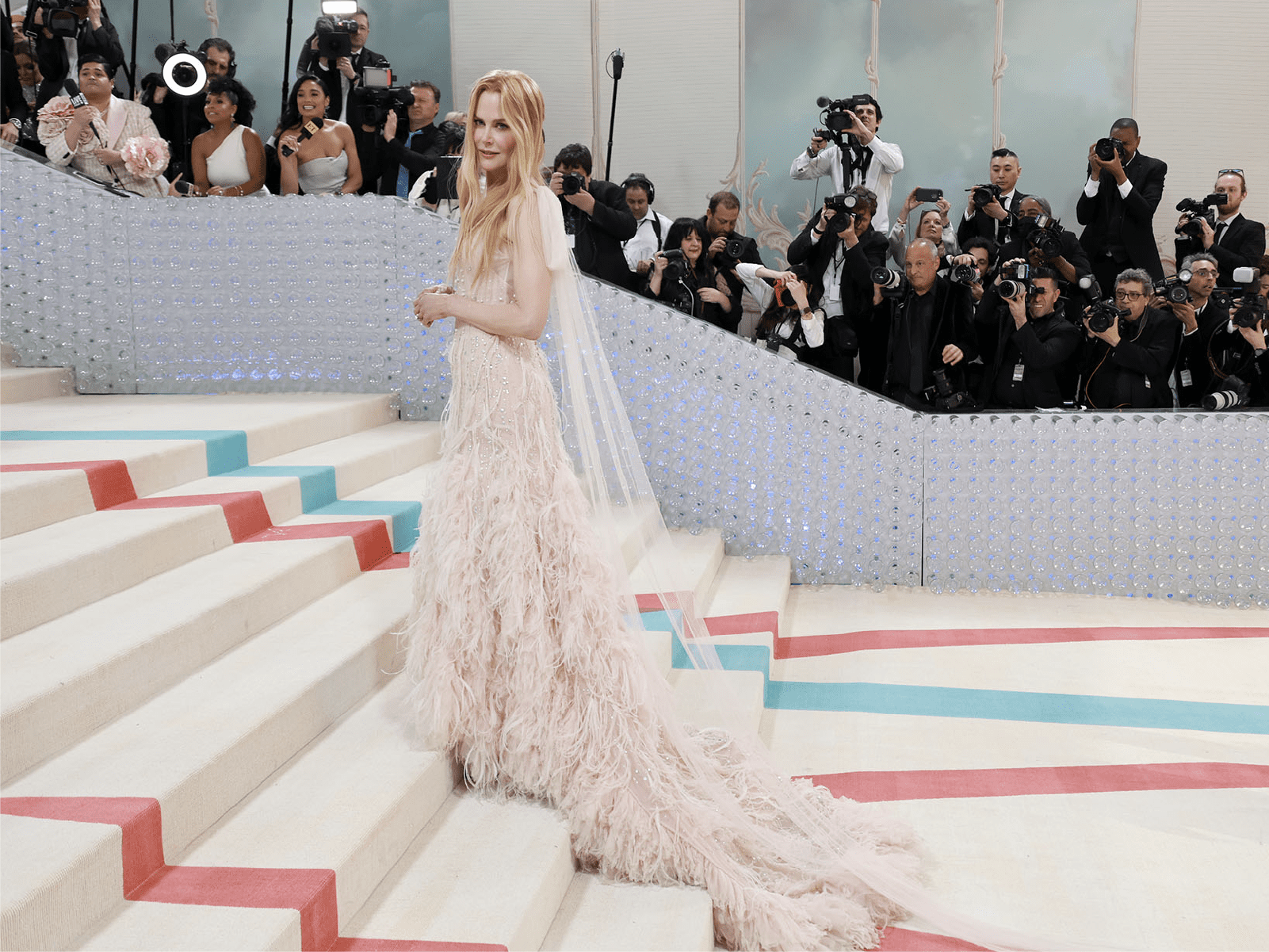 Actress Nicole Kidman poses on the staircase at the Met Gala wearing a feathered gown.