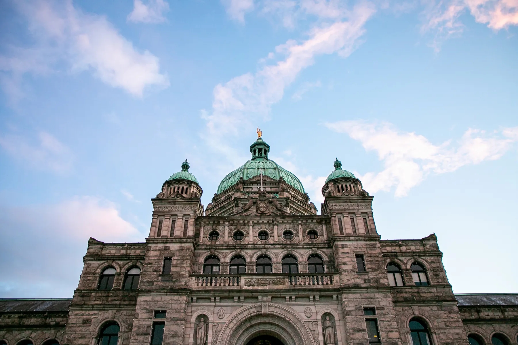 British Columbia's Legislature building seen from below, with sunny skies behind.