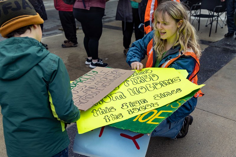 Sienna Nargang-White, a representative of SJC and second-year UBC student, hands out posters to a young attendee at the rally