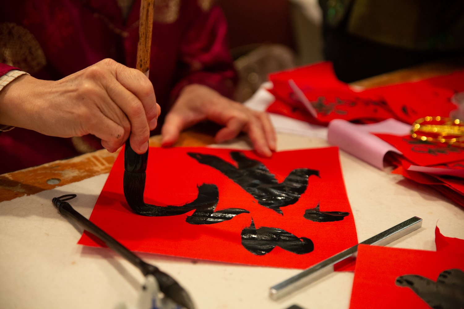 Chinese elders brush-lettered calligraphy on bright red banners for attendees to hang in their homes.