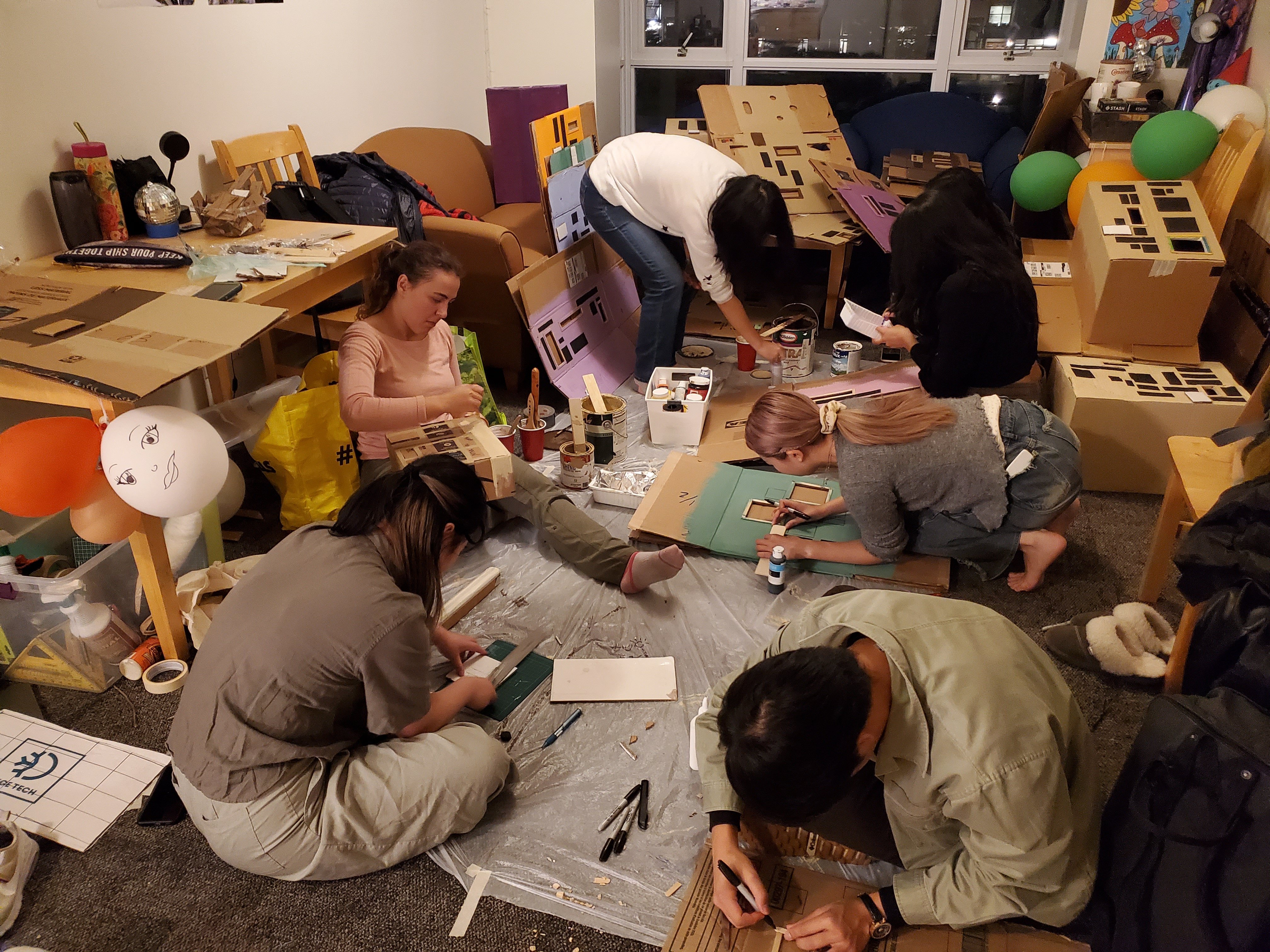 UBC Musical Theatre Troupe’s set build crew working on the early stages of painting and attaching details to cardboard houses.