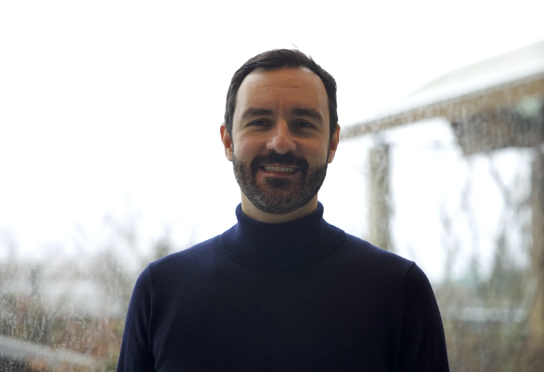 Igor Drljača wears a black turtleneck and smiles at the camera on the top floor of the Nest in front of the rooftop garden.