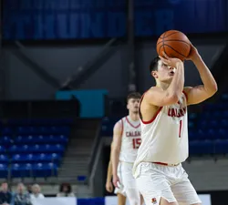 A man player in a white "Calgary" jersey aims for a free throw and the ball is in front of his face.