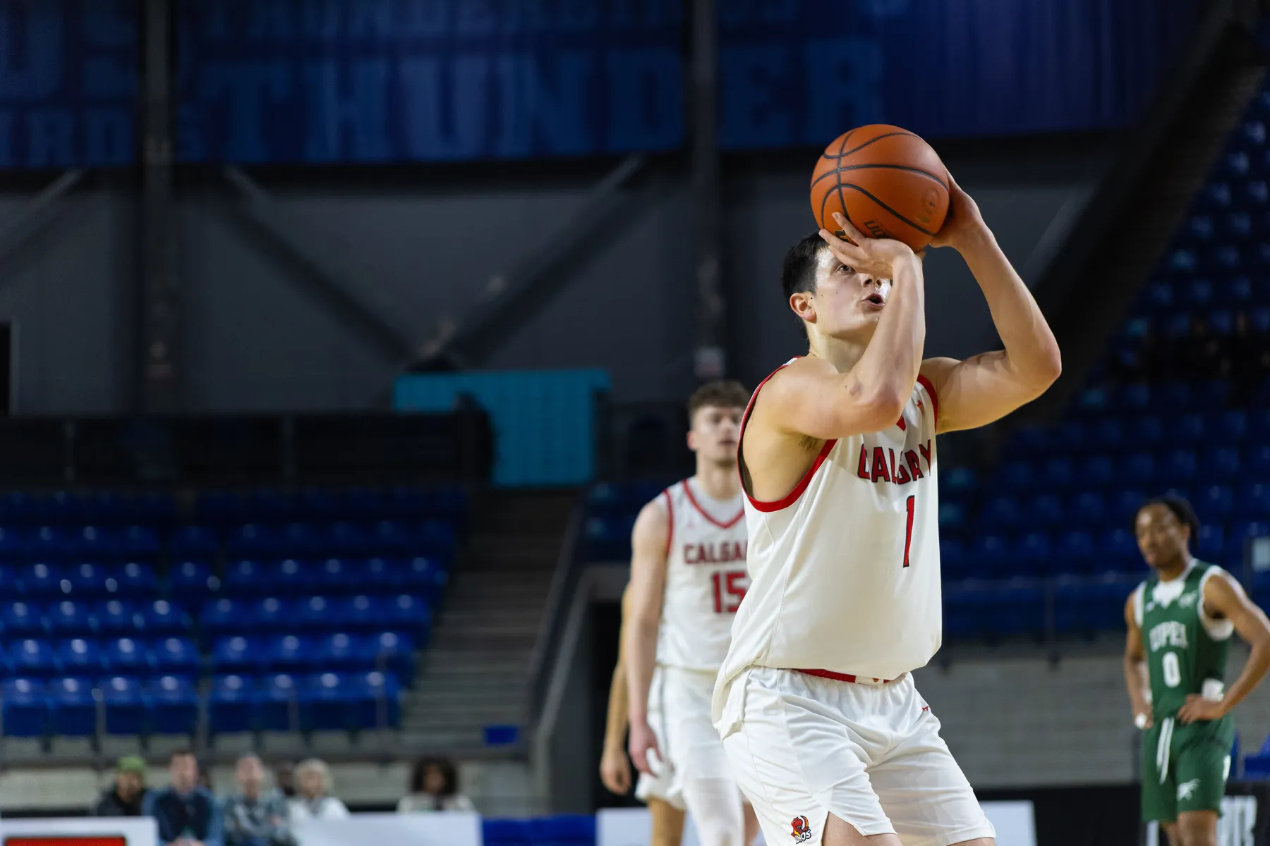 A man player in a white "Calgary" jersey aims for a free throw and the ball is in front of his face.