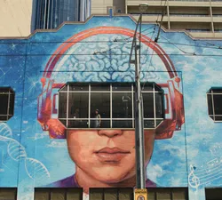 Shot from the exterior of a building with a brain-themed mural painted on the side, Radomski looks out a window.