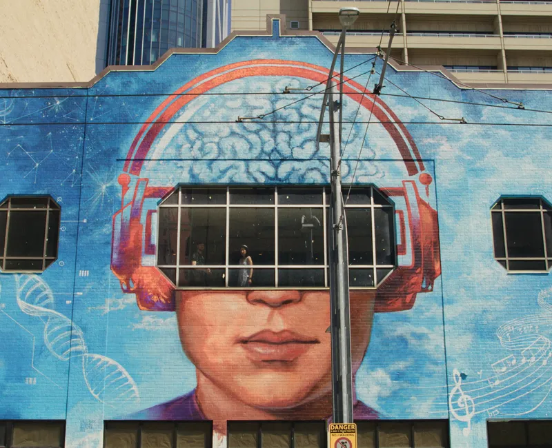 Shot from the exterior of a building with a brain-themed mural painted on the side, Radomski looks out a window.