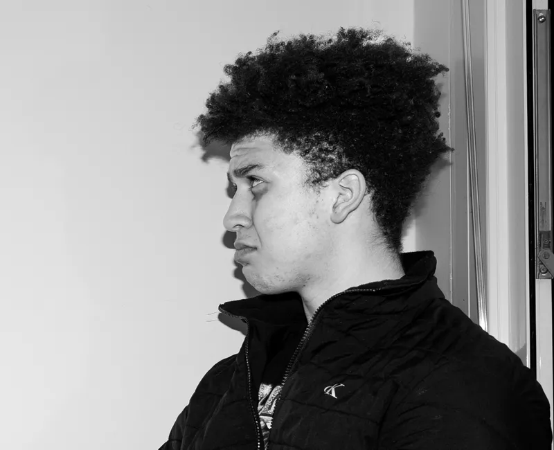 A greyscale image of a student sitting on a table and looking depressed.