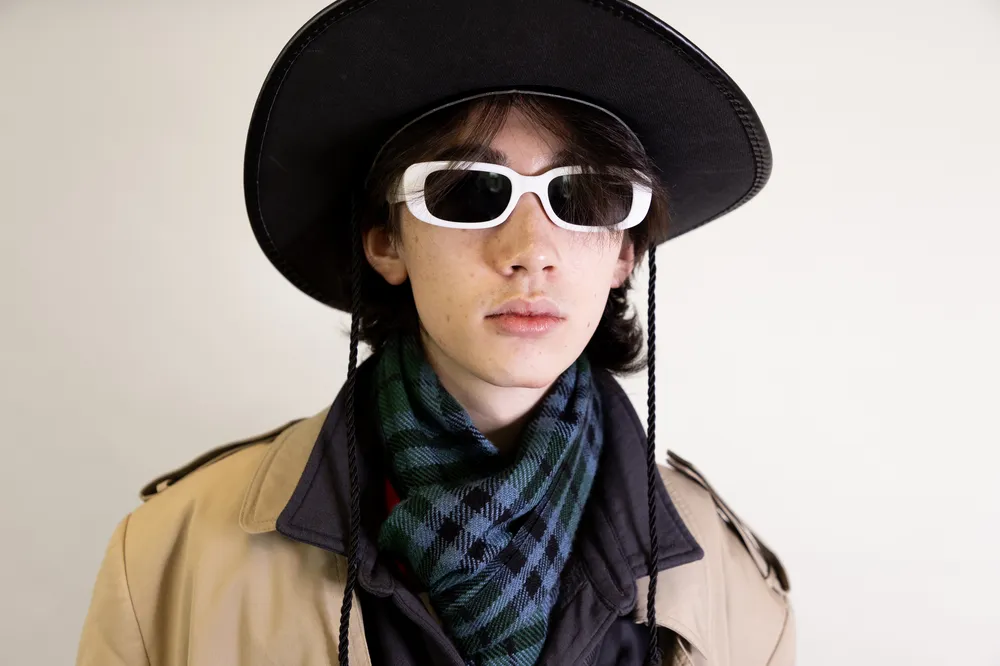 Somone with a blank expression wearing white frame sunglasses and a wide brim hat.