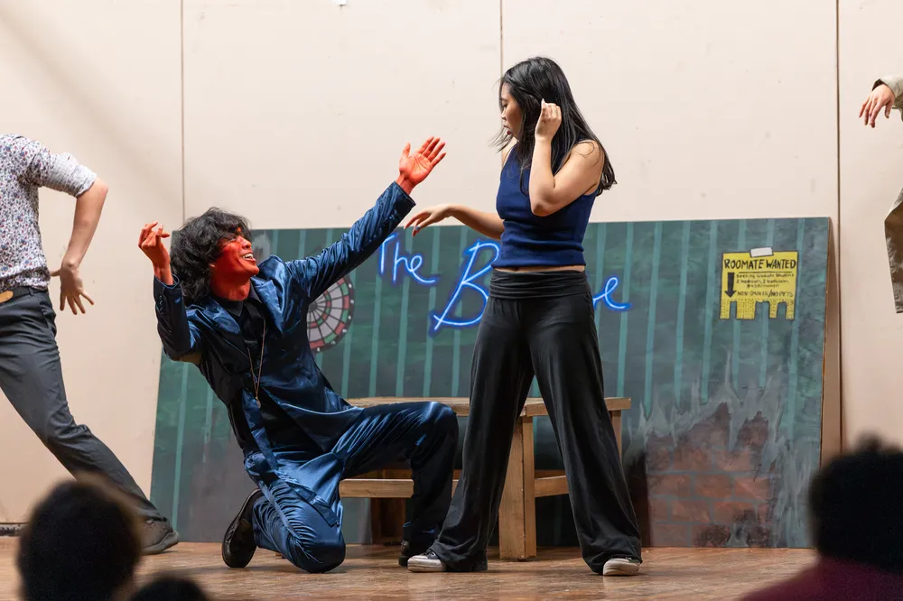 A man with orange face paint kneels on the ground next to a woman in blue and black
