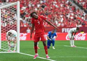 Manzambi dances to celebrate in front of Canada's net, while Canada's back line crouches over, distraught.