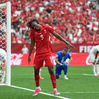 Manzambi dances to celebrate in front of Canada's net, while Canada's back line crouches over, distraught.