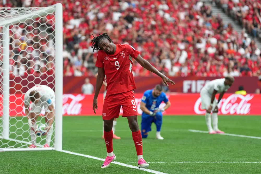Manzambi dances to celebrate in front of Canada's net, while Canada's back line crouches over, distraught.