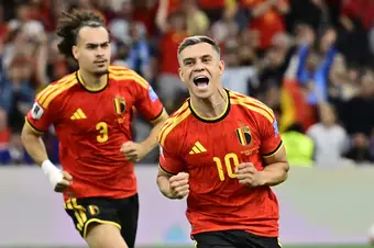 Trossard runs forward, celebrating his goal, while a teammate follows close behind